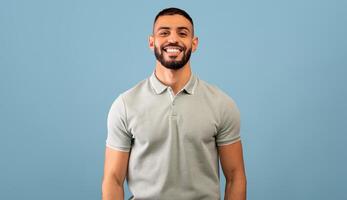 Portrait of happy arabic guy smiling at camera over blue studio background, copy space. Handsome middle-eastern young man in casual showing positive emotions photo