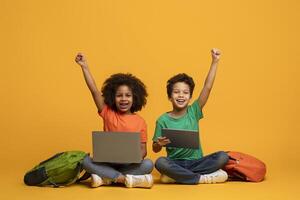 Two African American children, a boy and a girl, are sitting on the floor with laptop and digital tablet in front of them, raising hands up, yellow background photo