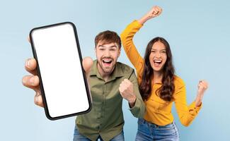 A man and woman are seen holding up a cell phone with white blank screen. Both individuals are smiling as they interact with the device, demonstrating modern communication and technology usage. photo