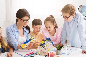 A teacher and four students are working together to build a robot in a classroom setting. All focused on the task at hand, with the teacher guiding the students and helping them with the assembly photo