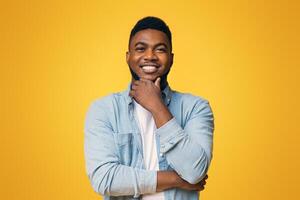 Portraif of handsome bearded african american man touching his chin and smiling over yellow studio background, copy space photo