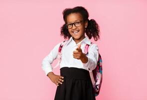 Hey, you. Cute Afro Elementary Student Girl Pointing Finger At Camera On Yellow Background In Studio. Copy Space photo
