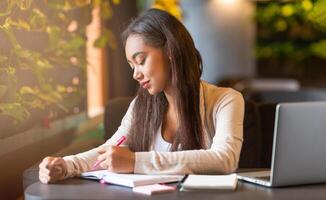 A young black girl is seated at a table, concentrating as she writes in a notebook. Her pen moves swiftly across the paper, capturing her thoughts and ideas in the quiet setting. photo