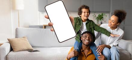 A joyful African American family interacts at home, with a child playfully seated on a parent shoulders, while another parent holds up a smartphone, capturing a happy moment together. photo