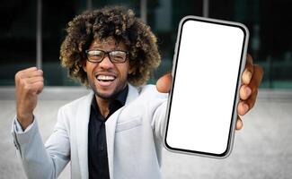 African American man dressed in a suit standing while holding up a cell phone, looking at the screen intently. He appears focused and engaged in whatever is displayed on the device. photo