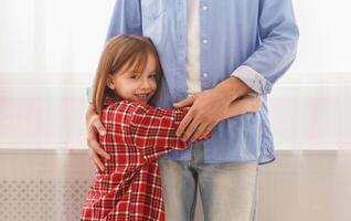 You are my hero. Sweet smiling little girl hugging her dad at home, staying next to window, close up, copy space photo