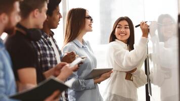 Girl showing answers on whiteboard in classroom with classmates standing around photo