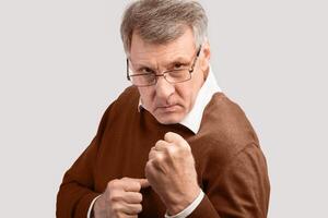 Aggressive Senior Man Clenching Fists Standing In Ready-To-Fight Position Looking At Camera Over Gray Studio Background. photo