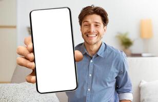 A smiling man holds a smartphone with a blank white screen, looking directly at the camera. photo