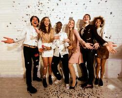 Party Mood. Excited Millennials Students Standing Showered With Confetti Having Fun Celebrating Event Against White Wall Indoor photo