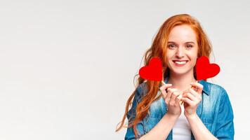 A woman is standing and holding two heart-shaped objects in front of her face, panorama with copy space, white background photo