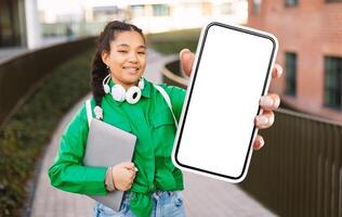 A girl wearing a green jacket is standing and holding up a cell phone. She appears to be looking at the screen intently. photo