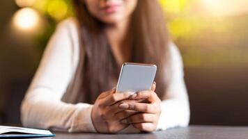Cropped of girl is seated at a table, focused on her smartphone screen. She appears engrossed in whatever she is viewing on the device, with her attention fully captured by the screen. photo