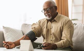 Hypertension In Older Age. Senior Black Man Measuring Arterial Blood Pressure Having Problems With Tension, Using Blood-Pressure Cuff Sitting On Sofa At Home. Healthcare And Medicine Concept photo