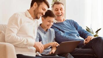 Male Family Weekend. Joyful Boy Using Laptop Computer Sitting Between Father And Grandpa On Sofa At Home. Panorama photo