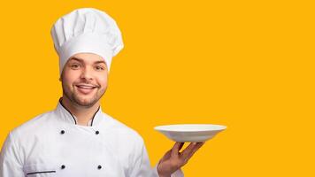 Smiling Chef Man Serving Dish Holding Empty Plate Standing Over Yellow Background. Studio Shot photo