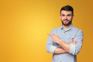A man with crossed arms standing in front of a bright yellow background, pointing at copy space for advertisement photo