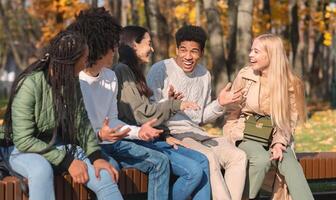 Black cheerful guy telling his multiracial friends funny story, spending time together in public park photo