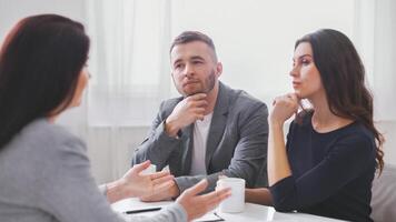 A couple sits across from a financial advisor in an office setting, discussing their finances. They appear to be listening intently to the advisor, who is speaking to them directly. photo