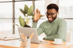 Happy African businessman making call to family using laptop during coffee break in office, copy space photo
