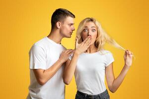 Unbelievable. Guy whispering secret or gossip to surprised girl, yellow background with copy space photo