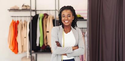 African American woman is standing in front of a rack filled with various clothes. The rack is neatly organized with different types of clothing displayed. photo