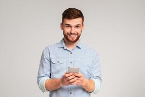 Young bearded man using his phone and smiling on studio background, websurfing or scrolling, copy space photo