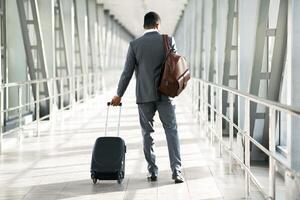 A corporate traveler with luggage is seen at an airport. The mood is focused and professional, with a modern airport setting that emphasizes travel and business, back view photo