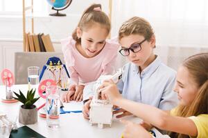 Three young children are working on a science project in a classroom. The children are collaborating on a mechanical project, building a robot or machine together photo