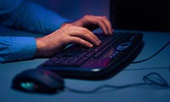 A close-up photo of a mans hands typing on a black computer keyboard. The image is taken from a low angle, with the keyboard in focus and the mans hands slightly blurred.