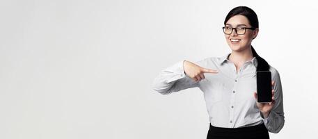 Smiling Business Girl Pointing Finger At Smartphone Empty Screen On White Studio Background. Empty Space photo