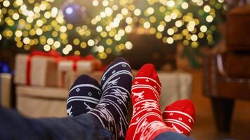 Couple relax. Two pair of feet in colorful ornamented Christmas socks over blurred Xmas room background, selective focus photo