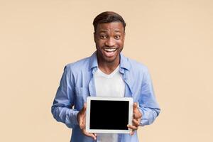 Excited Black Man Holding Digital Tablet With Empty Screen Standing In Studio Over Yellow Background. Mockup photo
