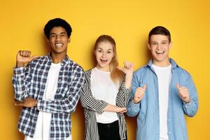 Three multiethnic teenagers are standing side by side, each with a beaming smile and giving a thumbs-up gesture photo
