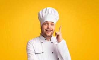 Great Recipe. Excited Chef Man Pointing Finger Up Having Idea Of A New Dish Standing On Yellow Studio Background. Panorama photo