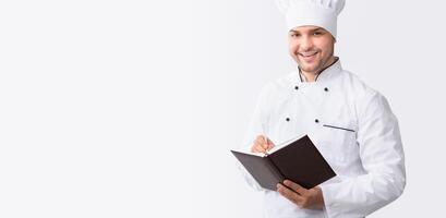 Culinary Book. Chef Guy Writing Recipes Standing In Studio Over White Background. Panorama With Empty Space photo