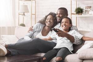 Happy african american family relaxing and watching tv at home, enjoying weekend together. photo