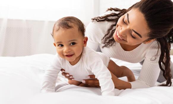 contento africano americano mamá abrazando bebé niñito participación infantil como él gateando en cama gasto hora juntos, jugando y unión en dormitorio a hogar. maternidad y niño cuidado rutina concepto foto