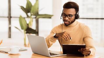 Serious African American Support Operator With Headset Looking At Laptop, Writing Documentation. Empty space photo
