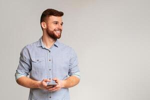 Young man blogger using his phone and looking away on copy space, isolated on grey studio background photo