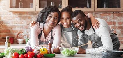 Happy african family embracing at kitchen while making healthy dinner, copy space photo