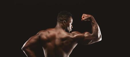 A muscular man flexes his bicep while standing against a black background. photo