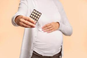 Unrecognizable Pregnant Lady Showing Pills Blister Pack Touching Belly Posing Over White Studio Background. Shallow Depth, Cropped photo