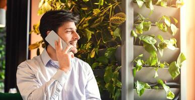 Handsome man talking on phone and smiling at modern cafe, looking at empty space, sun flare, panorama photo