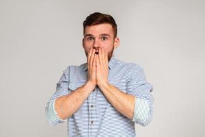 Surprised guy. Shocked man holding his hands hiding open mouth on grey studio background, copy space photo