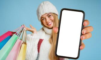 Happy young woman in white hat recommending credit card, posing with colorful shopping bags and smiling at camera, yellow background photo