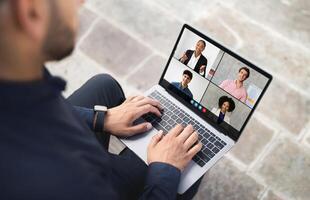 A person participates in a virtual meeting with four colleagues displayed on a laptop screen, highlighting remote work collaboration and communication. photo