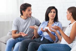 Misunderstanding In Friendship. Three Angry Friends Having Quarrel Arguing Sitting On Sofa At Home. Selective Focus photo
