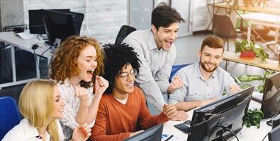 Cheerful emotional team enjoying victory, reading winning results on computer monitor in office, empty space photo