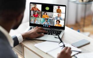 African American businessman sits at his desk and participates in a conference meeting on his laptop. He is listening intently to the speakers on the screen photo